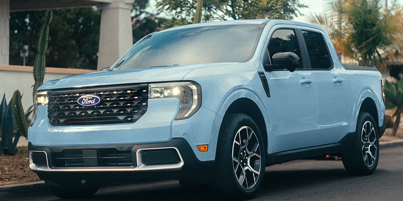 Light blue Ford pickup truck parked near a house with desert plants, featuring a modern design with sleek lines and a prominent front grille.