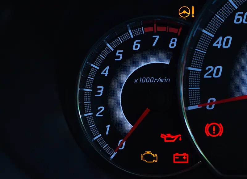 A close-up view of a car's tachometer and warning lights on the dashboard, showing the RPM gauge and various alert indicators.
