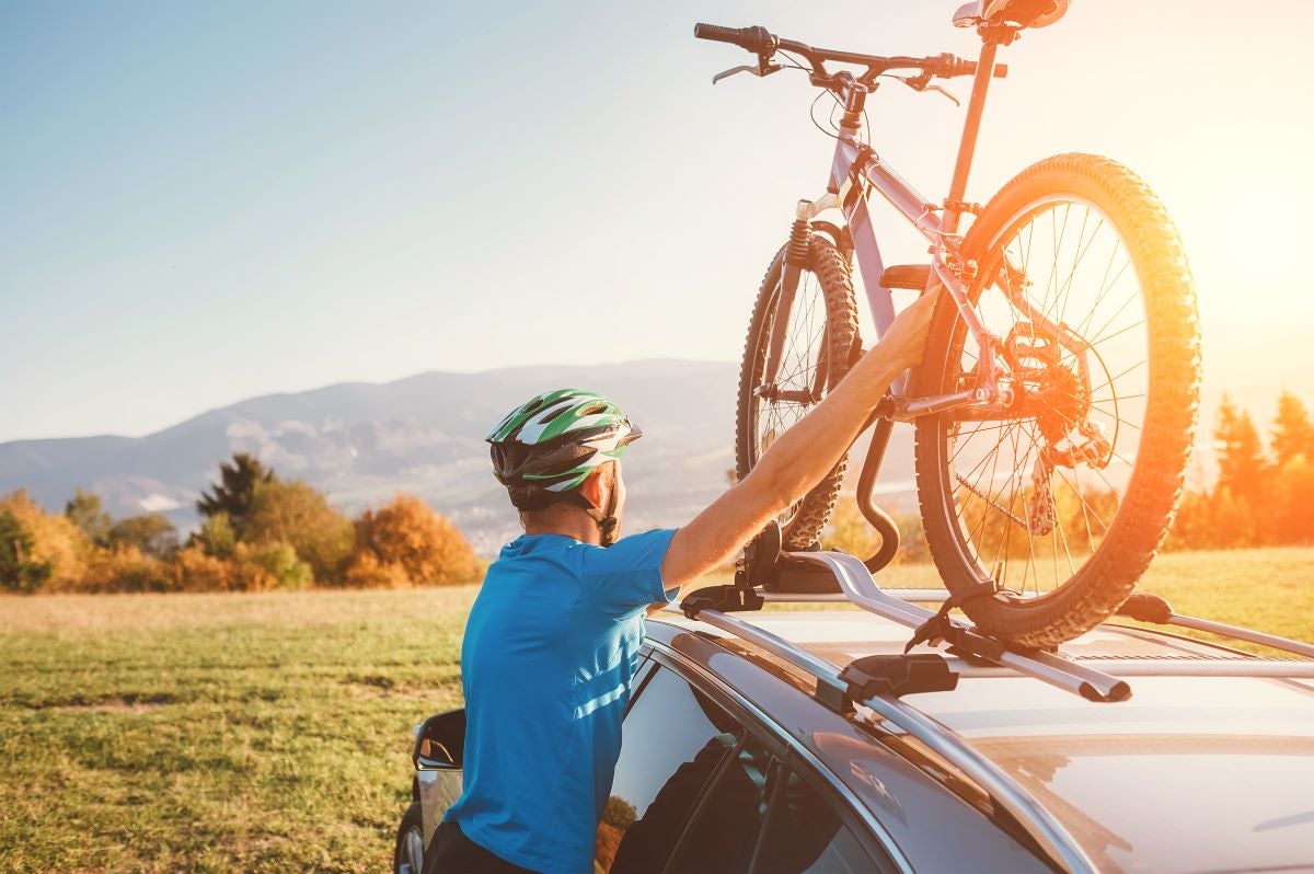 A man places his bicycle on the roof of his car, ready for an outdoor adventure.